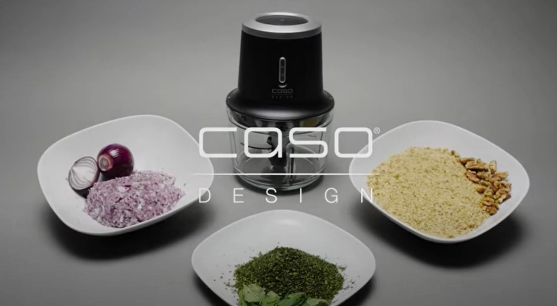 Food processor with ingredients on plates, onions, nuts, and herbs.