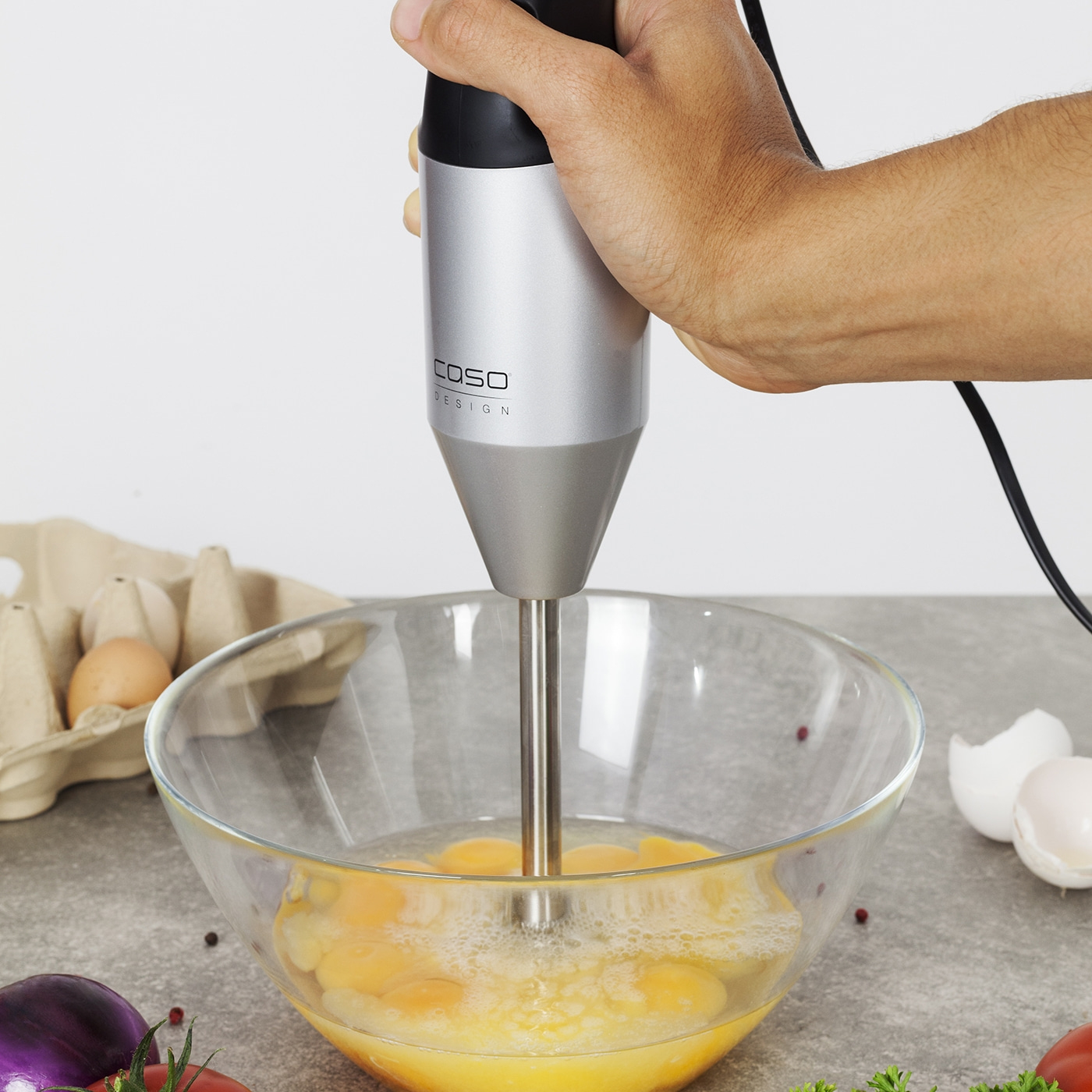 Hand hält Stabmixer über Schüssel mit Eiern, die geschlagen werden.