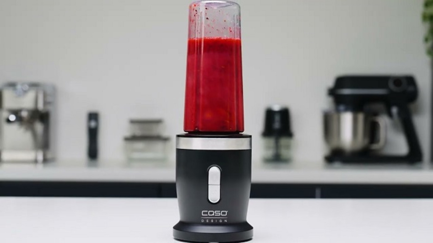 Black blender with red contents on a white surface in a kitchen.