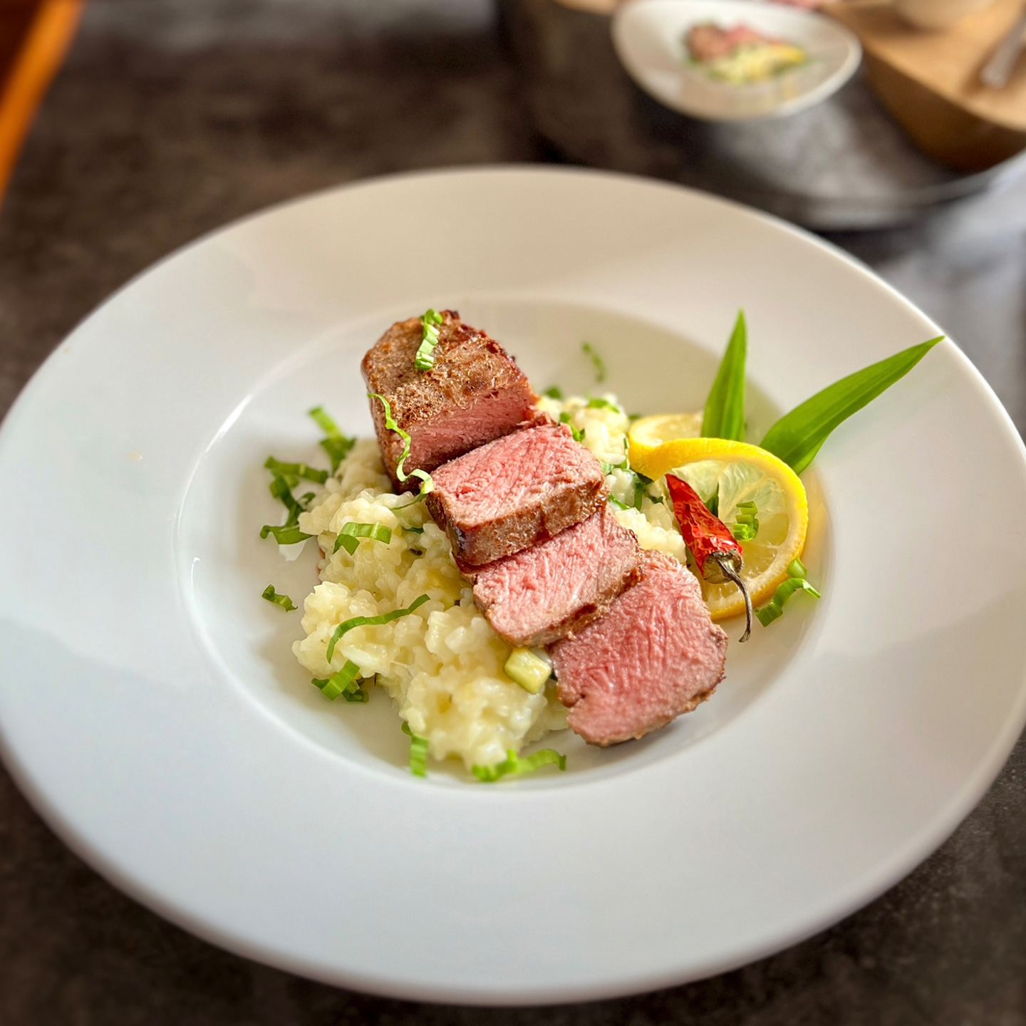 Sliced steak on rice with lemon and chili on a white plate