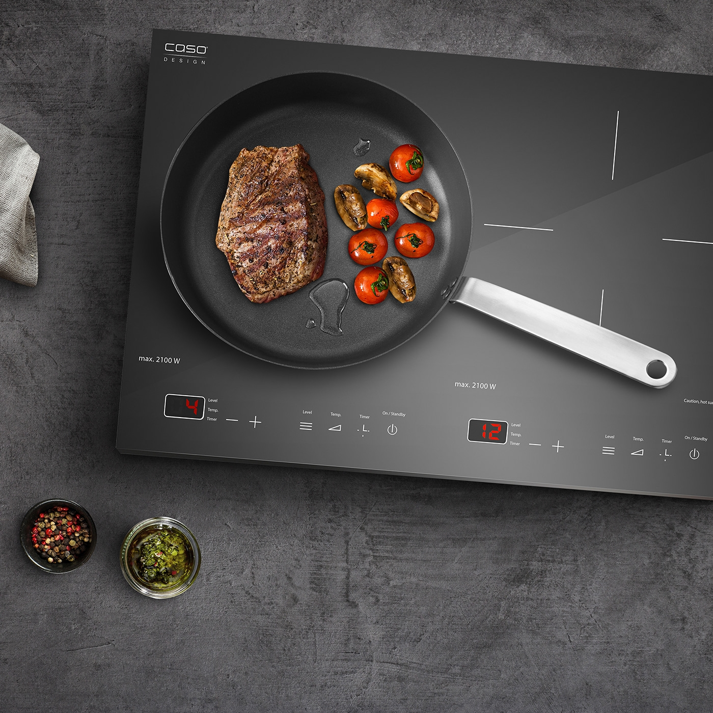 Induction cooktop with steak, tomatoes, and herbs, ready for cooking.