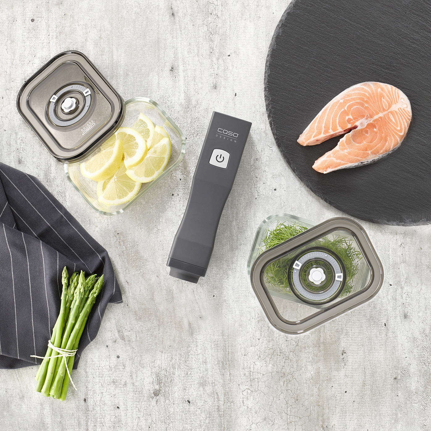 Fresh salmon, lemon, asparagus, dill, and vacuum sealer on a gray background.