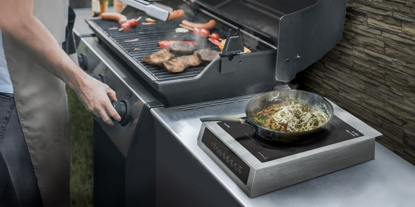 Grill mit Kochfeld und Essen. Person dreht am Grillregler.