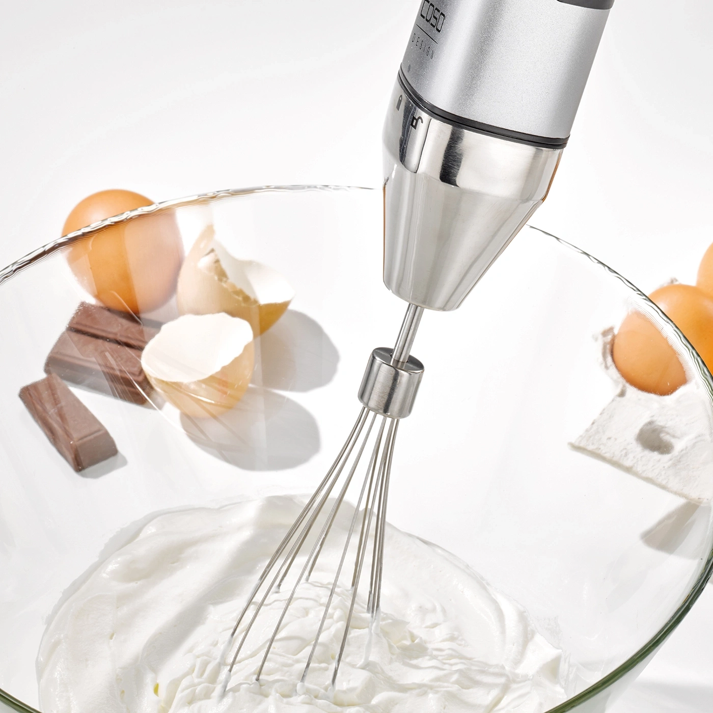 Handmixer in einer Schüssel mit Sahne, Eiern und Schokolade