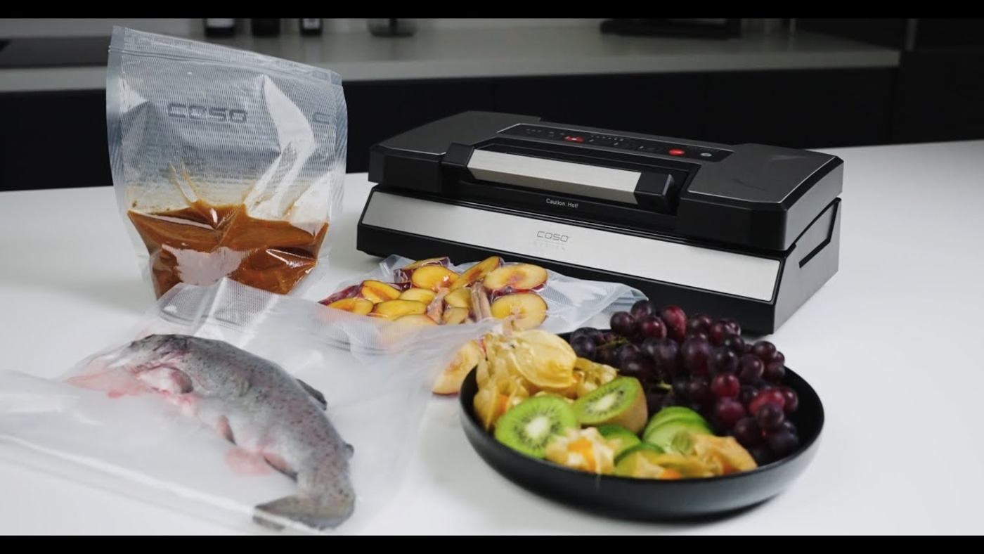 Vakuumiergerät mit Lebensmitteln in Beuteln und einer Schüssel mit Obst.