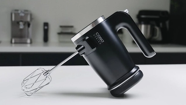 Black hand mixer on a white surface with Caso Design logo and a whisk.