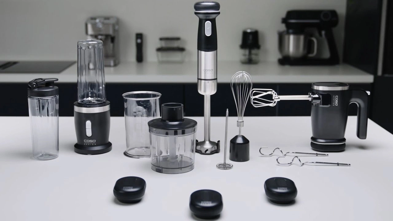 Kitchen appliances on white table: blender, immersion blender, whisk, hand mixer, accessories.