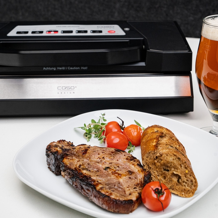 Gebratenes Steak mit Tomaten, Brot und Bier neben Vakuumiergerät.