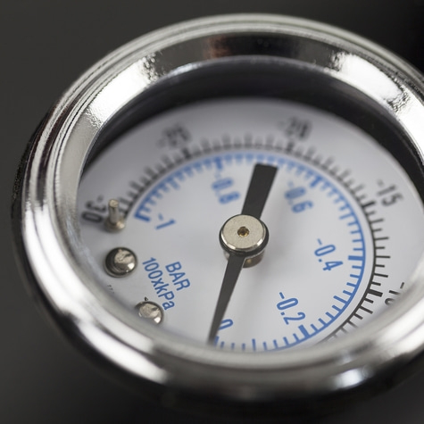 Close-up of a pressure gauge with a black needle and blue markings on a white dial