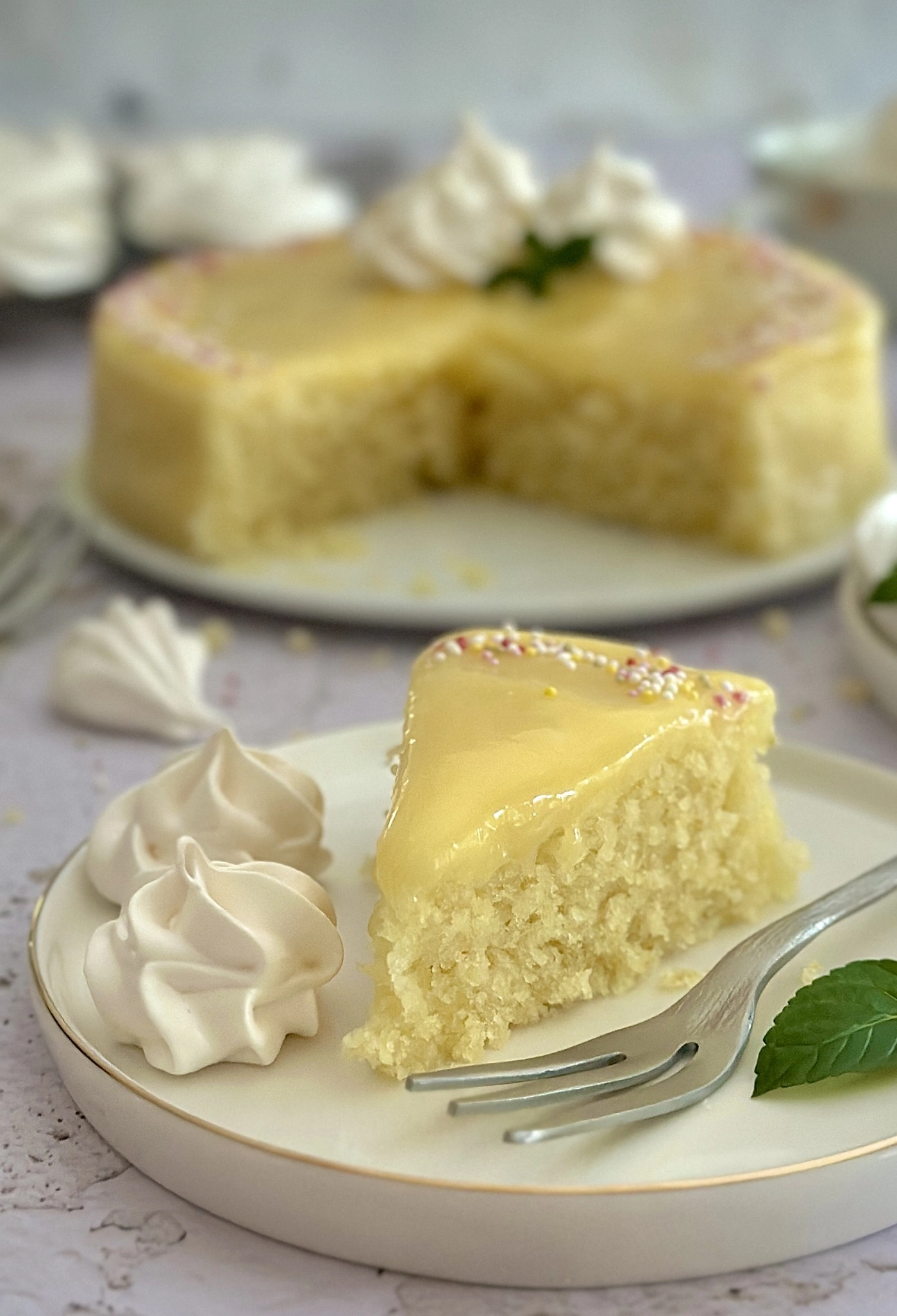 Slice of cake with glaze and sprinkles, next to meringue and fork on plate.