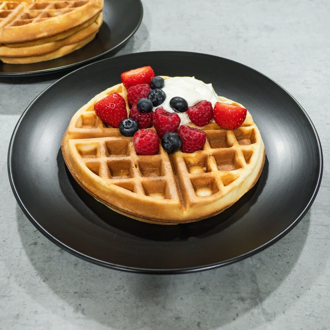Waffle with berries and cream on a black plate, close-up shot
