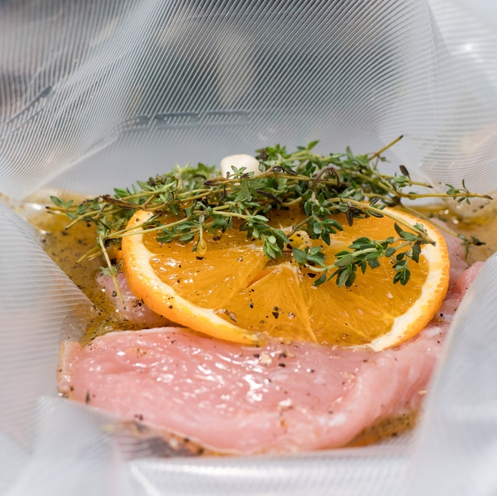 Rohes Fleisch im Vakuumbeutel mit Orangenscheibe und Kräutern, bereit zum Kochen.