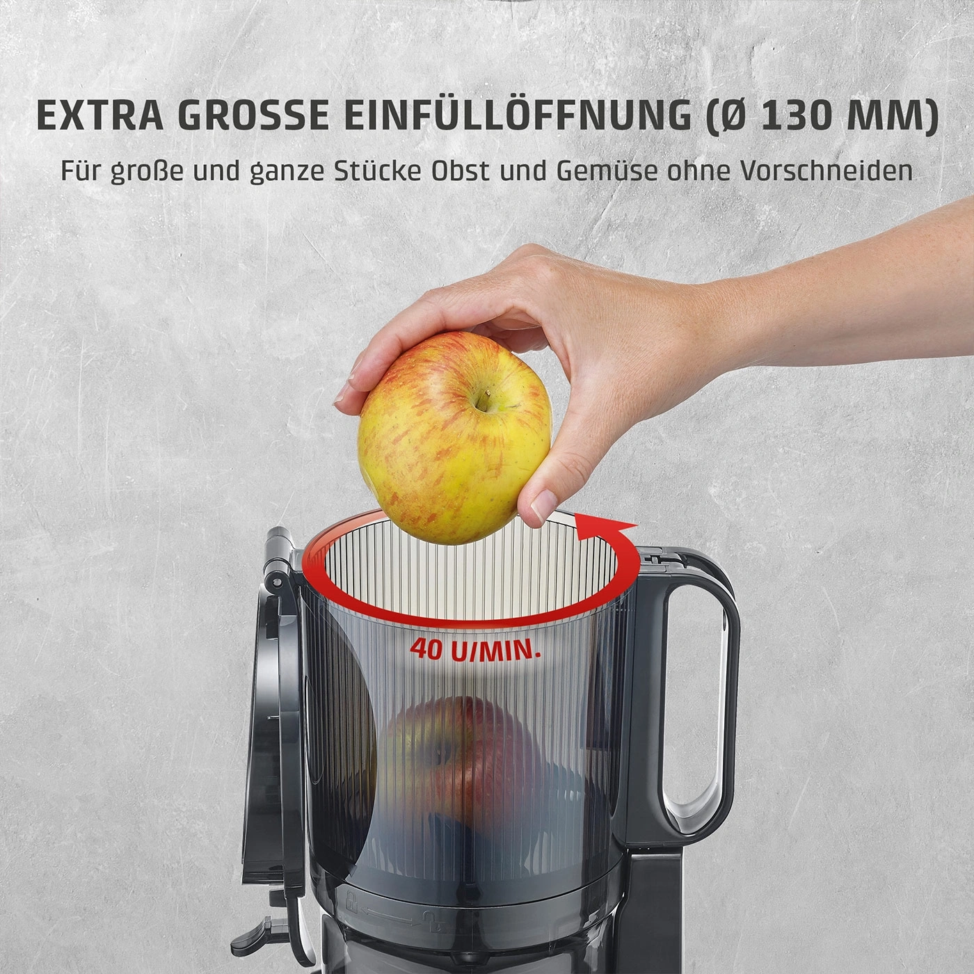 Eine Hand legt einen Apfel in eine große Einfüllöffnung eines Entsafters.