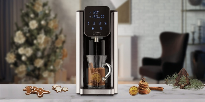 Hot water dispenser with cup, Christmas decorations and gingerbread on the table