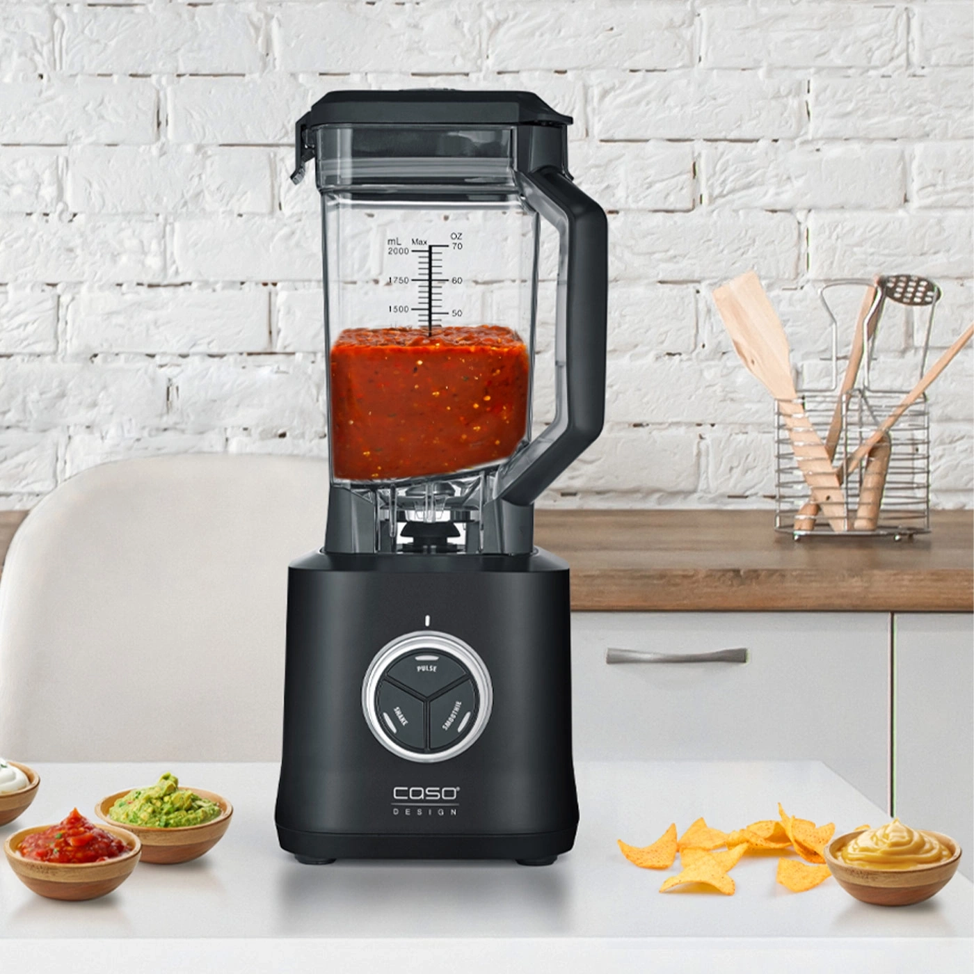 Black blender with salsa, guacamole, chips, and dips on a table setting.