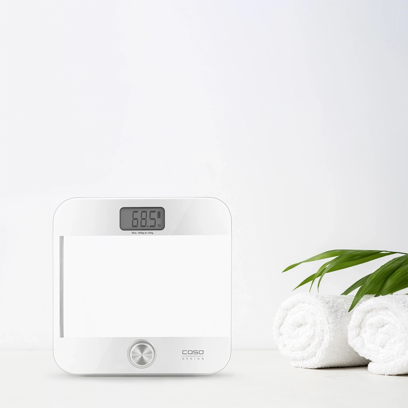 White scale displaying 68.5 kg, towels, and green leaves against a white background.