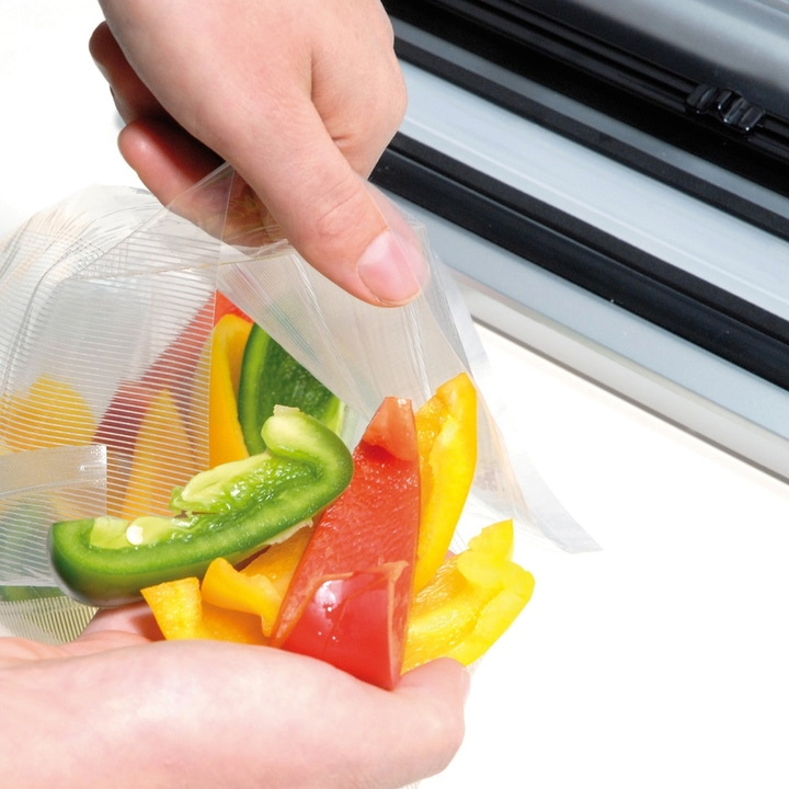 Person holding a bag of peppers in front of a vacuum sealing machine.