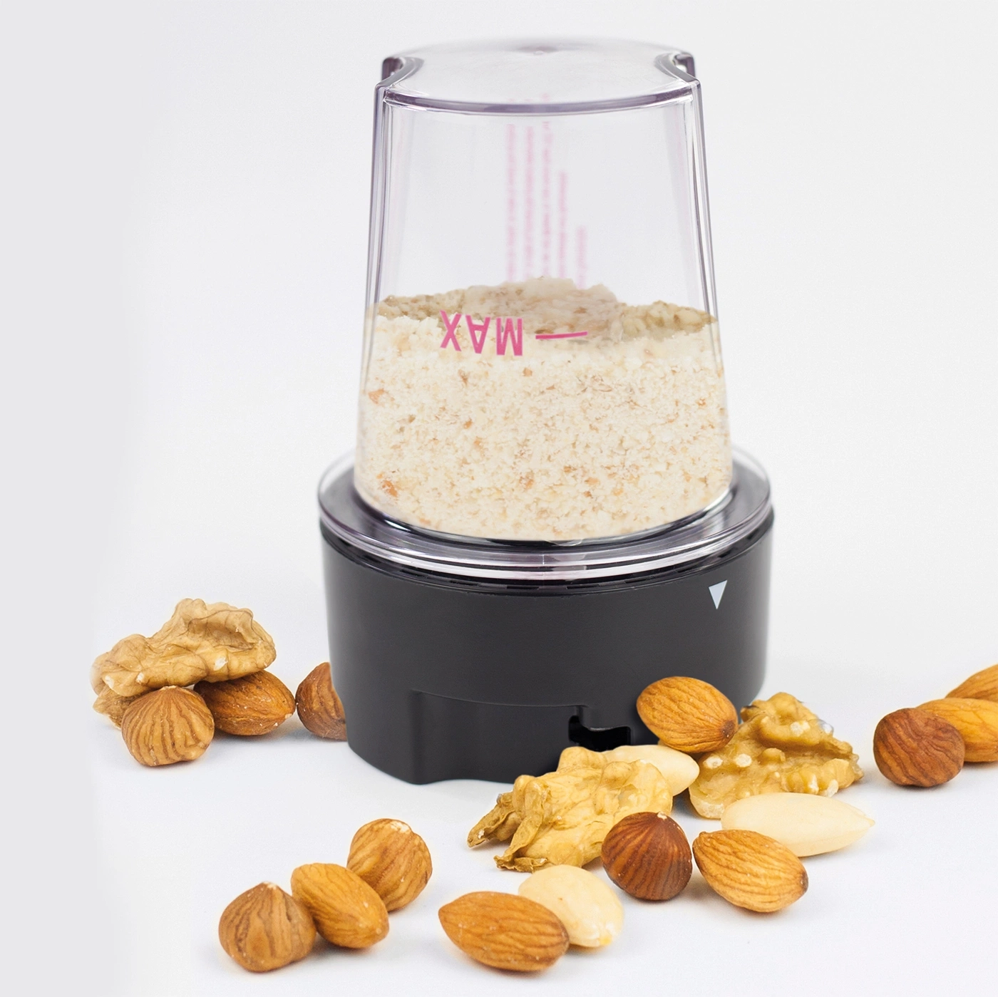 Nut grinder with nuts scattered on a white background, food preparation.
