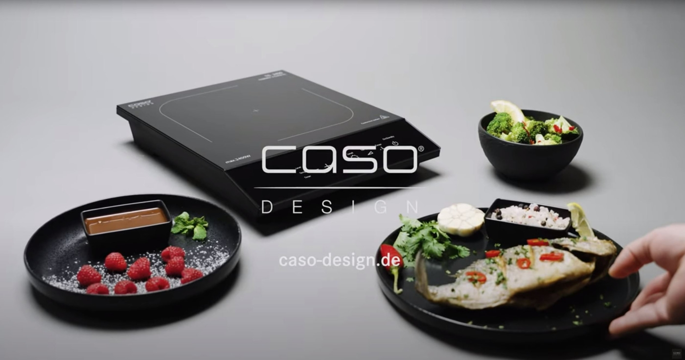 Induction cooktop with food, raspberries, broccoli and fish on black plate