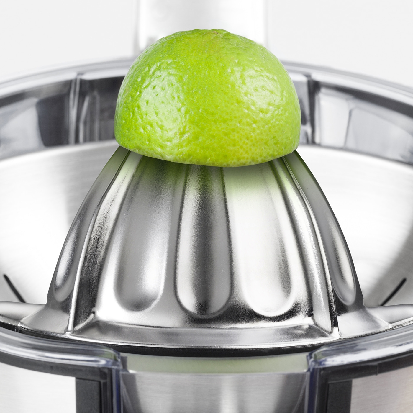 A lime on a citrus juicer. Close-up. Stainless steel. Green fruit.