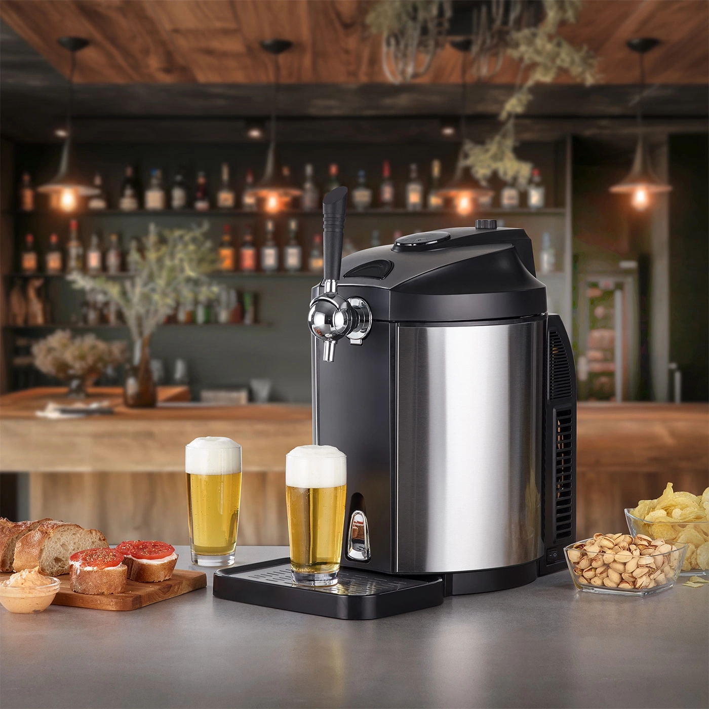 Bierkühler mit zwei Gläsern Bier, Snacks und Bar im Hintergrund.