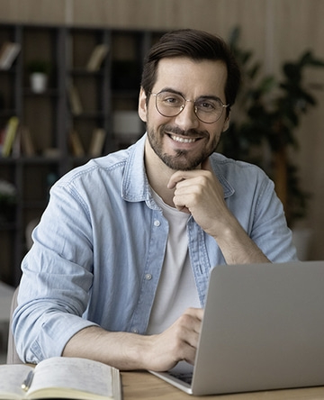 Ein lächelnder Mann mit Brille sitzt vor einem Laptop und lächelt.