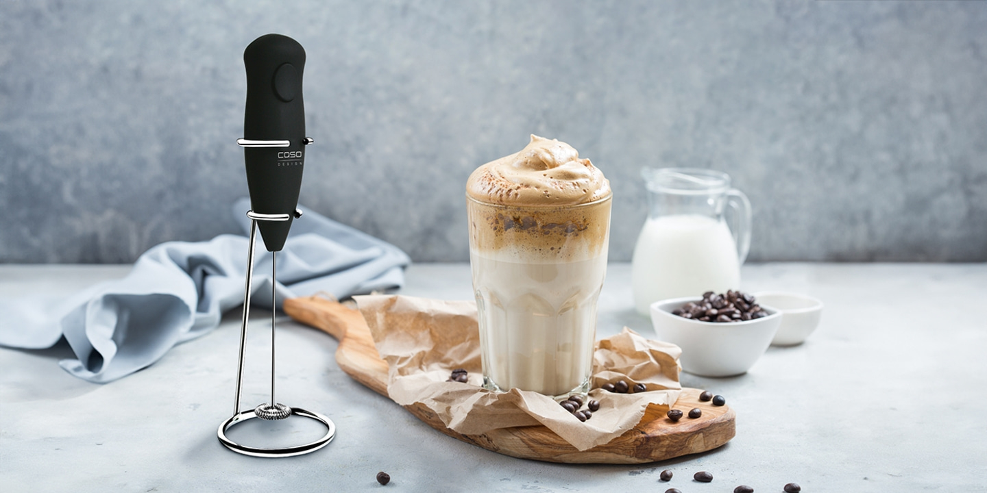 Kaffeegetränk mit Milch und Kaffeebohnen, daneben ein Milchaufschäumer.