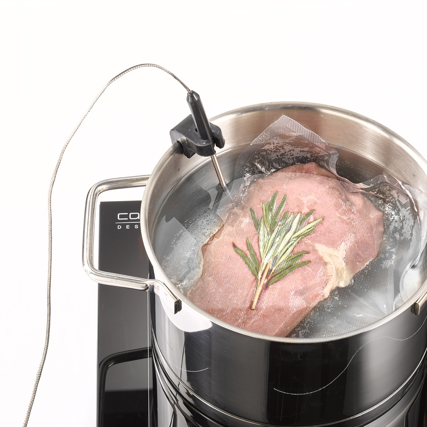 Meat being sous vide in a pot of water, with rosemary, and a thermometer.