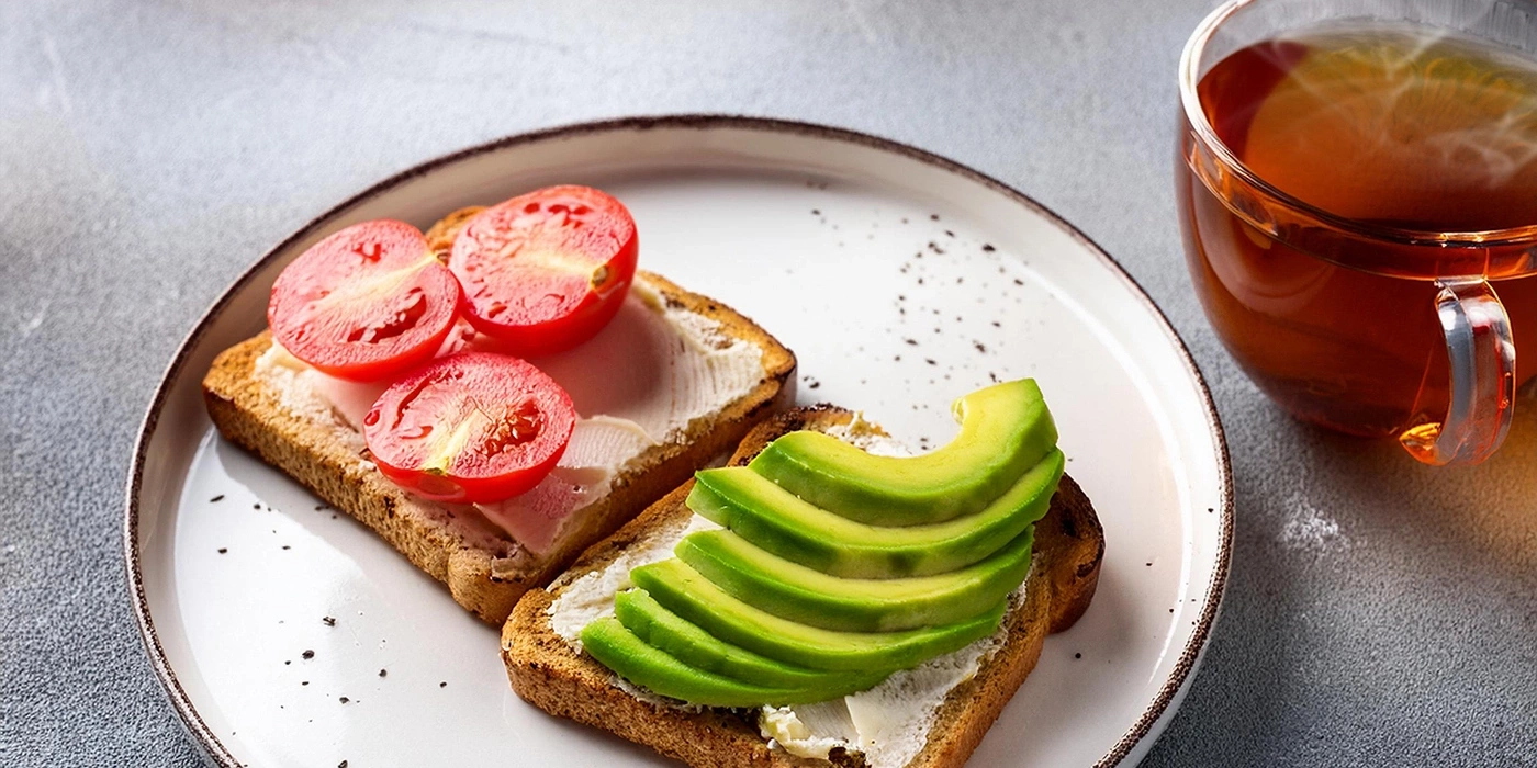 Geröstetes Brot mit Tomaten, Avocado und Tee auf einem Teller