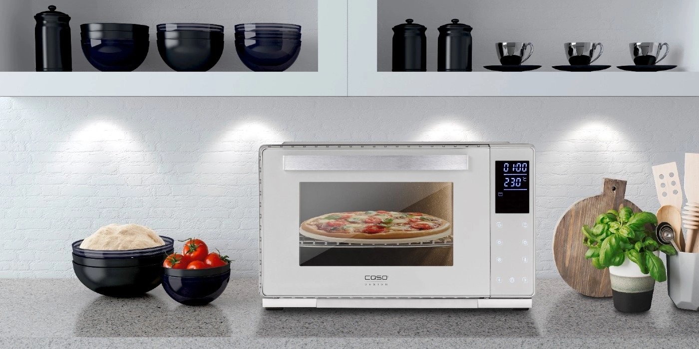 Pizza oven with pizza, ingredients, and kitchen utensils on a countertop.