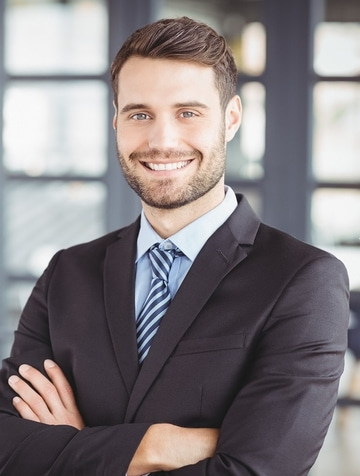 Ein lächelnder Mann im Anzug mit verschränkten Armen, im Büro.