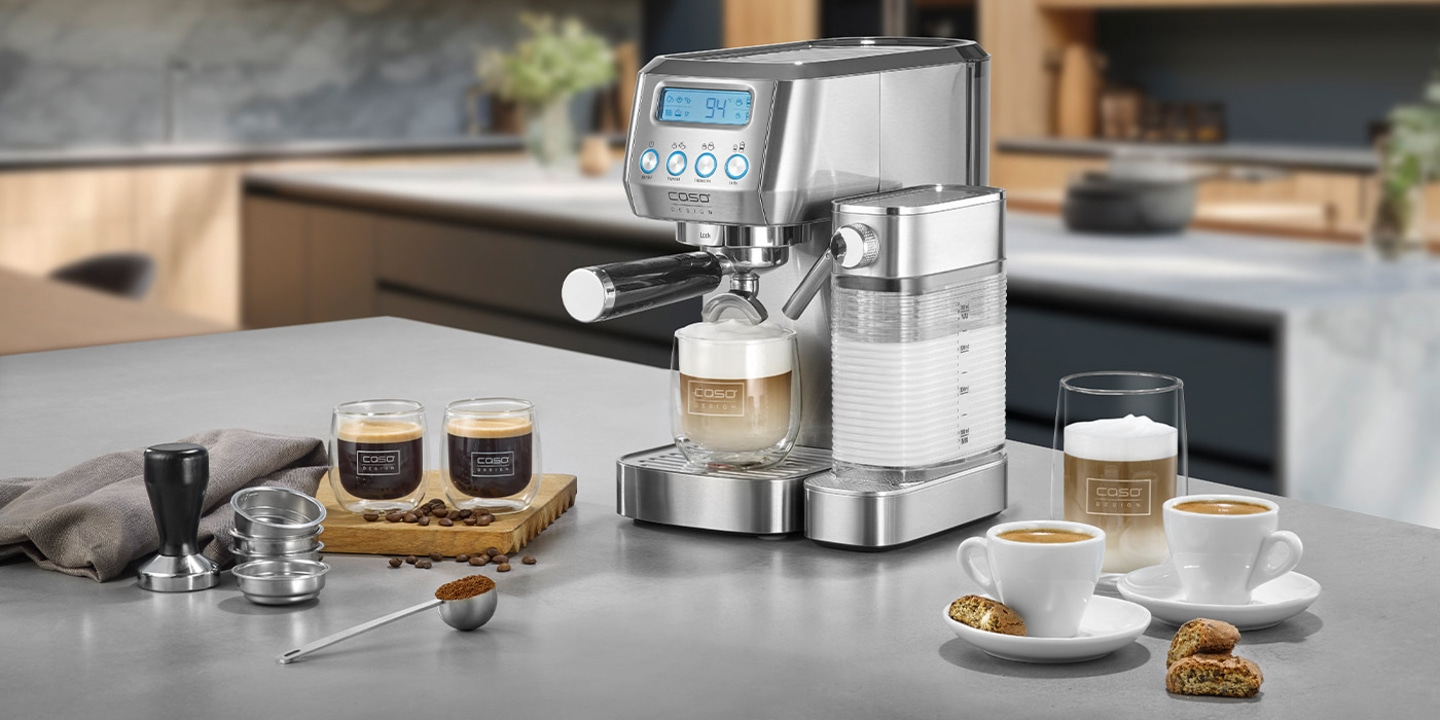 Kaffeemaschine mit Zubehör und Kaffeegetränken auf einer Arbeitsplatte in der Küche.