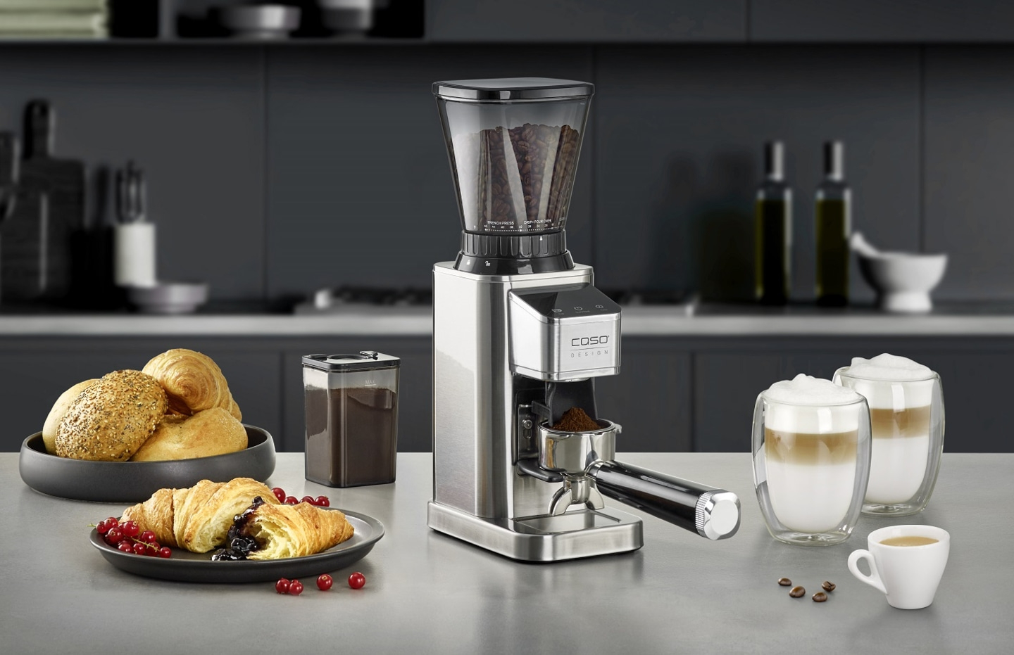 Kaffeemühle mit Kaffee, Croissant, Brötchen und Latte Macchiato auf dem Tisch