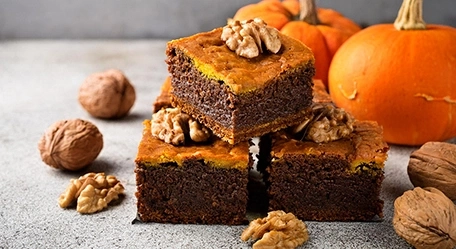 Köstliche Kürbiskuchen mit Walnüssen, dekoriert mit Kürbissen im Hintergrund.