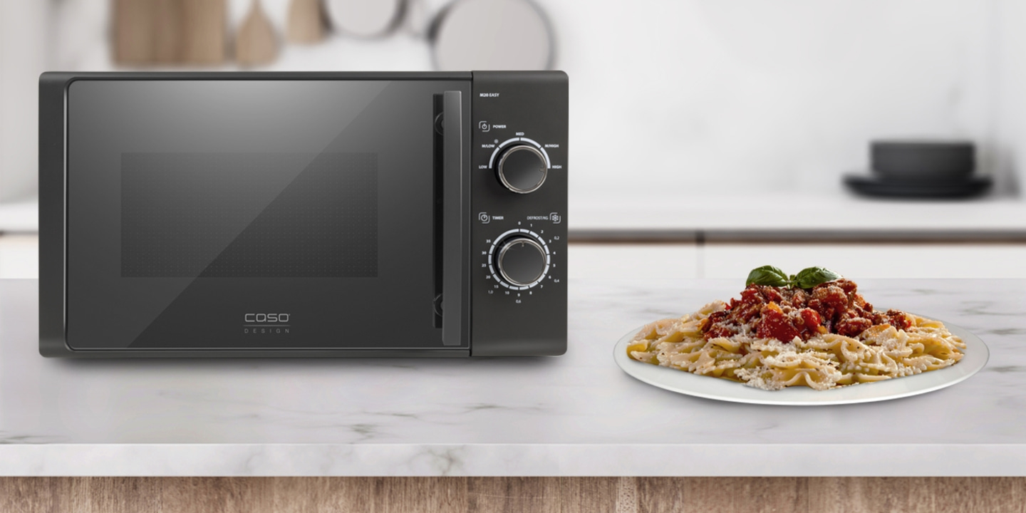 Mikrowelle und Pasta auf einer Küchenarbeitsplatte. Schwarze Mikrowelle und Essen.