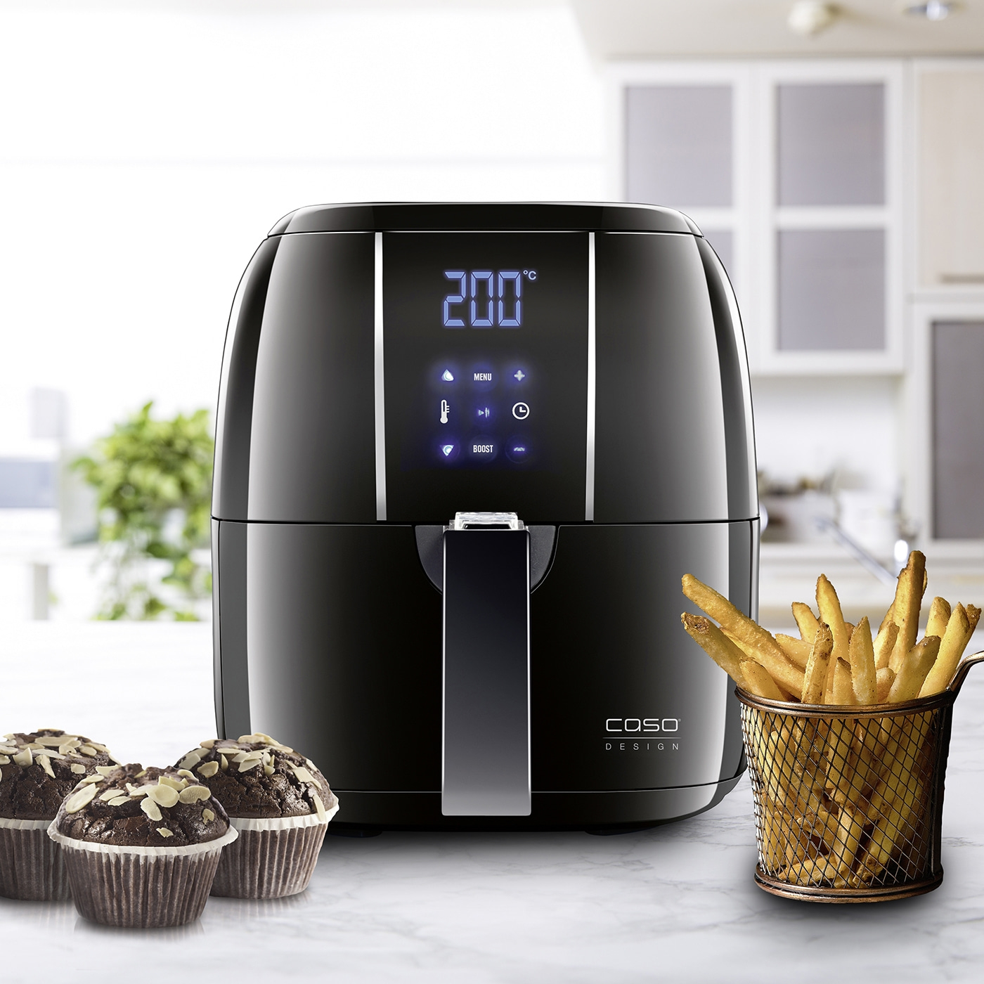 Schwarze Fritteuse mit Muffins und Pommes Frites auf weißem Tisch
