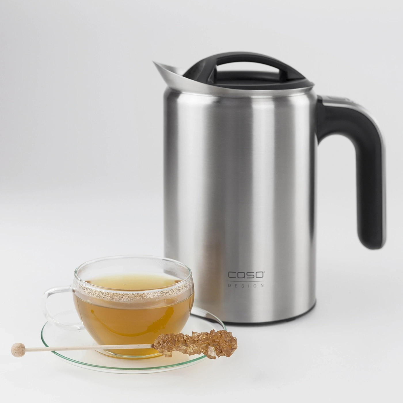 Teacup with tea and sugar stick next to a stainless steel coffee machine.