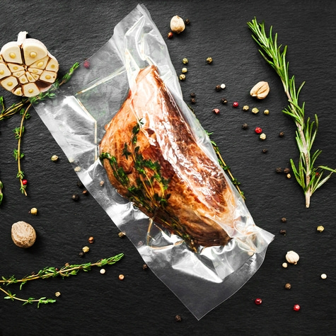 Meat in vacuum packaging with herbs and spices on a black surface