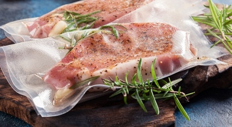 Vacuum-packed meat with herbs on a wooden board, close-up shot.