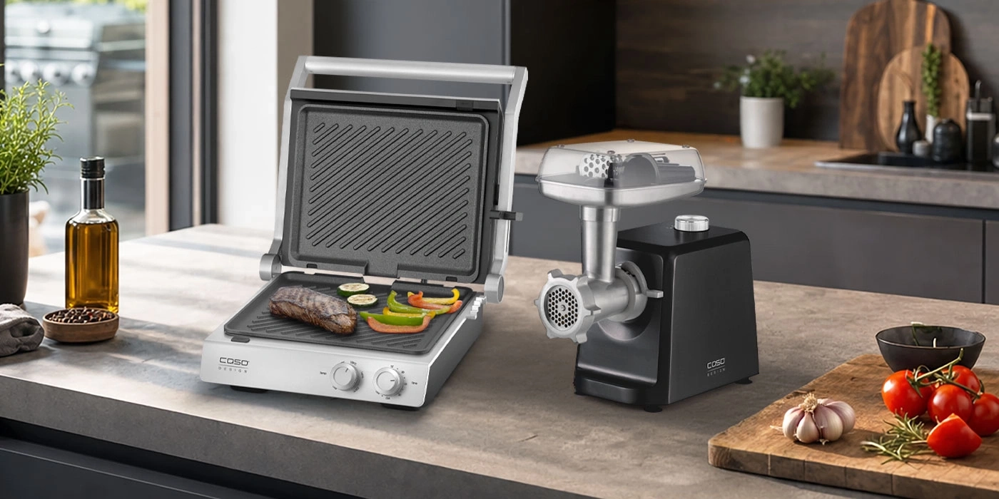 Ein Grill und ein Fleischwolf auf einer Arbeitsplatte in einer modernen Küche.