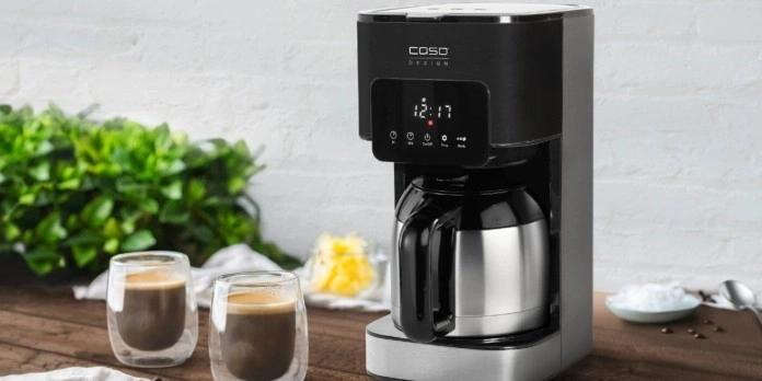 Kaffeemaschine mit zwei Kaffeegläsern auf einem Holztisch mit Grünzeug im Hintergrund.