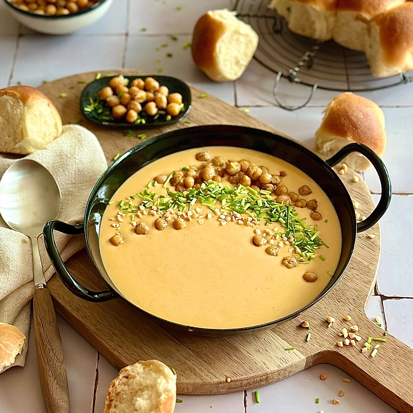 Kürbissuppe mit Kichererbsen, Brot und Kräutern auf Holzbrett