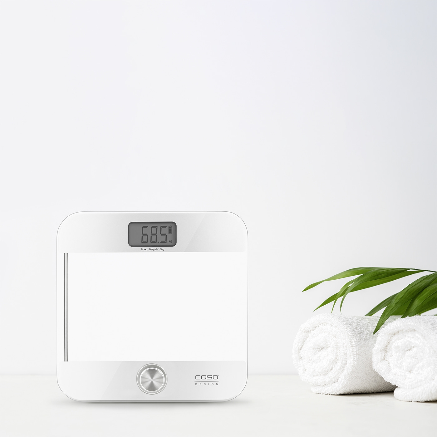 Weiße Waage mit Anzeige von 68,5 kg, Handtücher und grüne Blätter auf weißem Hintergrund.