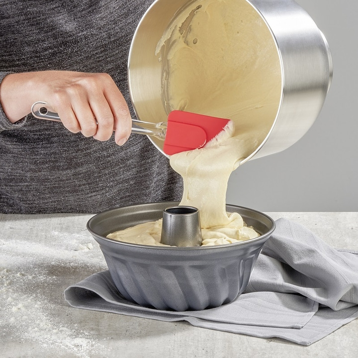Person pouring batter into a bundt pan with a red spatula