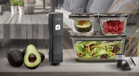 Avocado, Vakuumierer und Behälter mit Lebensmitteln auf einem Tisch im Freien.