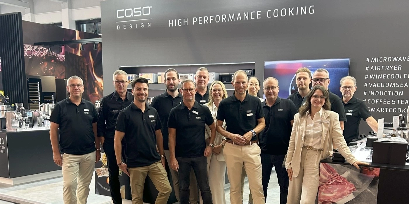 Gruppe von Personen, die vor einem Stand mit der Aufschrift COSO Design stehen.