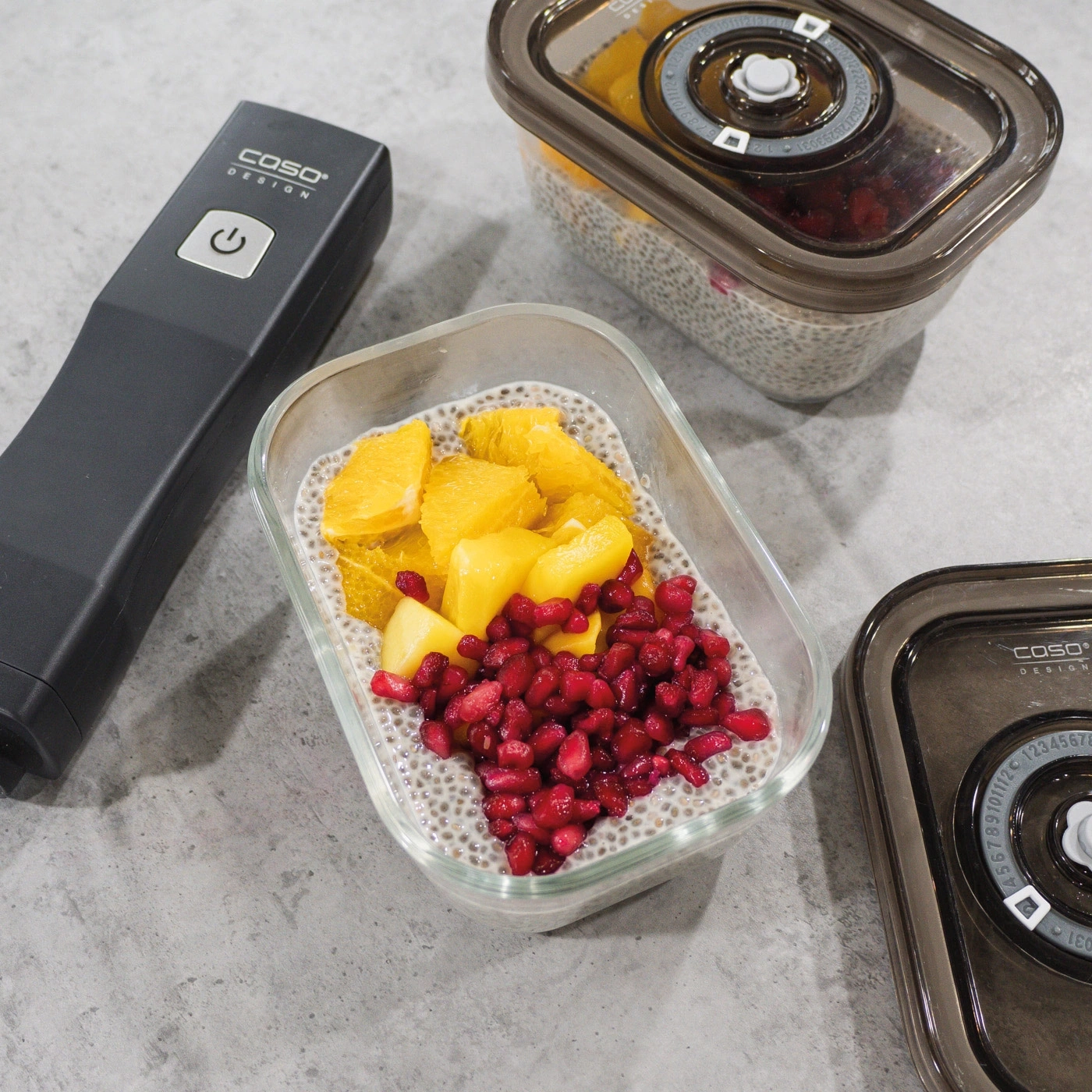 Fruits in glass containers with a vacuum sealer on a gray surface.