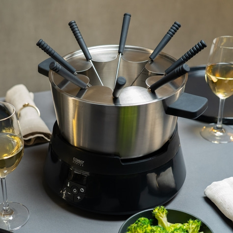 Fondue-Set mit Zubehör und Wein auf einem Tisch, bereit zum Essen.