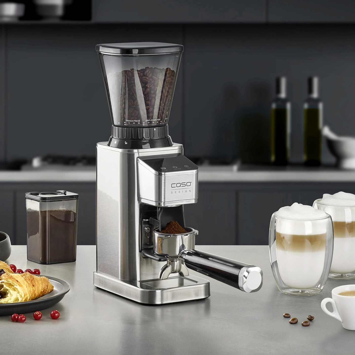 Kaffeemühle mit Zubehör, Kaffee und Gebäck auf einer Theke in einer Küche.