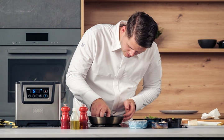Ein Koch bereitet Essen in einer Küche zu. Er kocht in einer Pfanne.